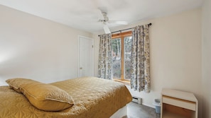 A bedroom with a bed, a ceiling fan, a window with curtains, and a small bedside table. - Chatiemac by Avantstay Wood Fireplace + Resort Pool + Game Room Ski Retreat (North Creek)