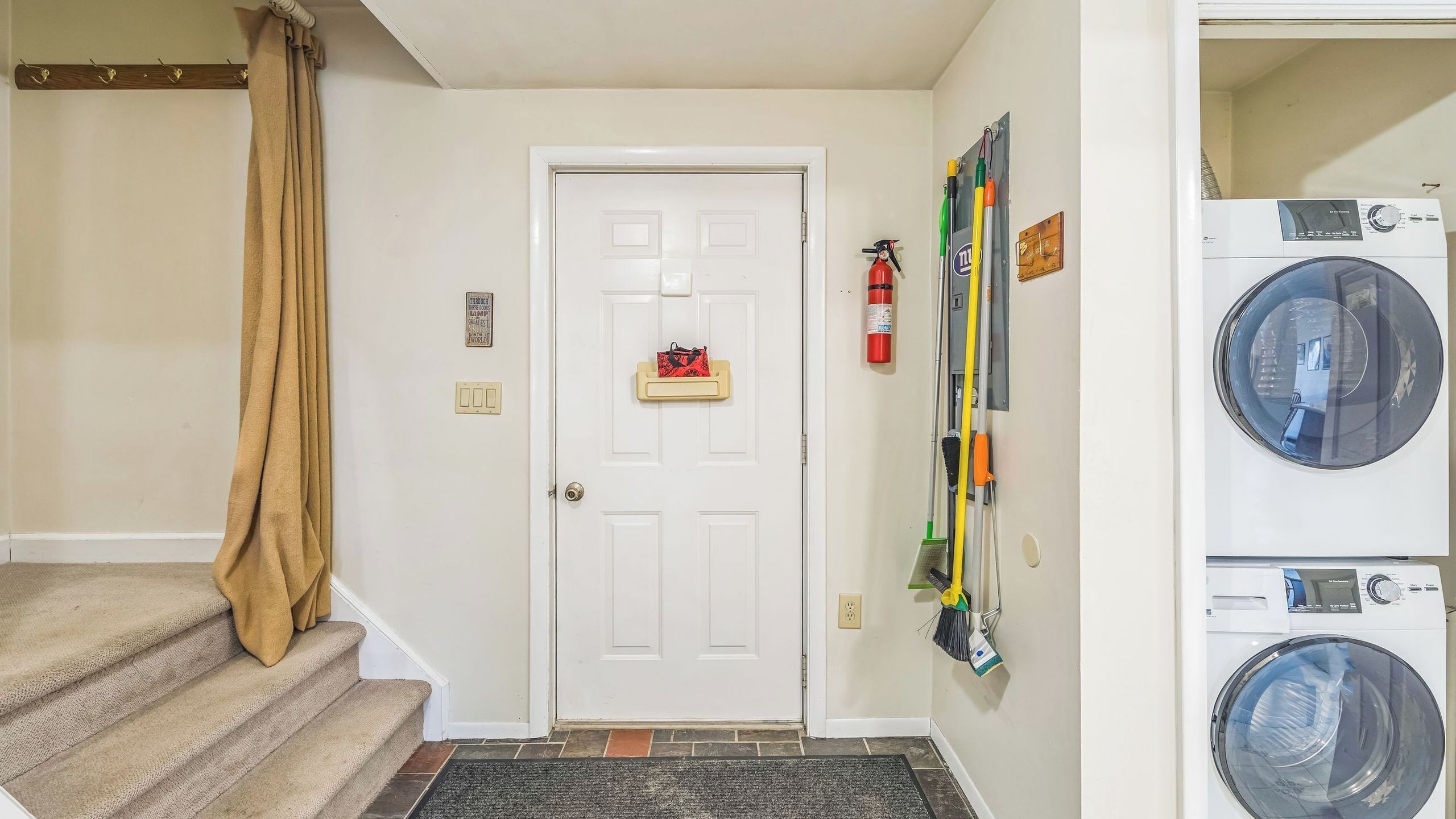A laundry area with a door, a fire extinguisher, and stacked washing machines.