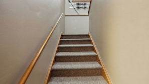 Ein Teppichbelag bedeckender Treppenaufgang mit Holzhandläufen, der zu einer Empore mit einer weißen Wand und einem Skiständer führt.