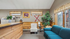 A reception area with a wooden desk, a white chair, a blue sofa, and a large window with a view. - Chatiemac by Avantstay Wood Fireplace + Resort Pool + Game Room Ski Retreat (North Creek)