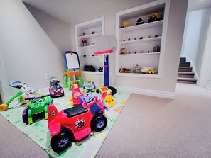 A playroom with various toys, a small basketball hoop, and shelves with toys. - Family Comfort Retreat (Brampton)