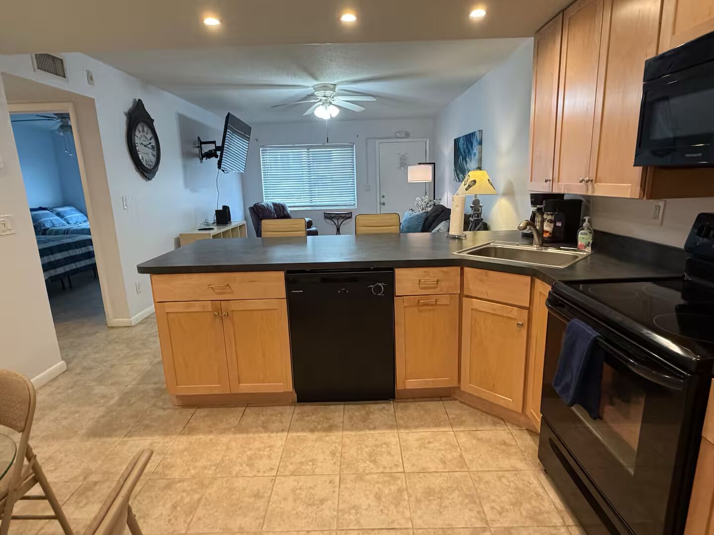 A kitchen with a central island, wooden cabinets, a black dishwasher, a stove, and a ceiling fan.