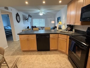 A kitchen with a central island, wooden cabinets, a black dishwasher, a stove, and a ceiling fan.