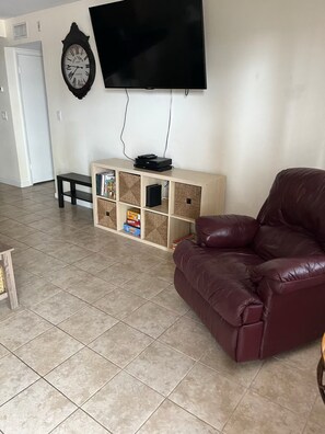 Ein Wohnzimmer mit Flachbildfernseher, einer Uhr, einer Holz-Unterhaltungseinheit, einem Ledersofa und einem Fliesenboden.