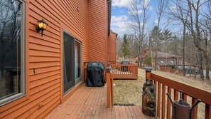 Eine Holzdielen-Terrasse mit Grill, einem Holzzaun und Blick auf einen bewaldeten Bereich.