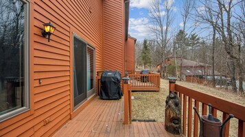 Une terrasse en bois avec un barbecue, une clôture en bois et une vue sur une zone boisée.
