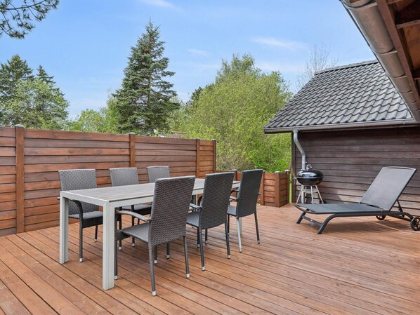 Eine Holzterrasse mit Tisch und Stühlen, einem Grill und einem Holzzaun.