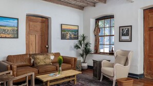 A living room with a brown leather sofa, a wooden coffee table, a wicker chair, and a potted plant. - Historic Rumpel Kammer - Steps to Main Street (Fredericksburg)