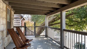 A wooden porch with two chairs, a railing, and a view of trees and a building. - Historic Rumpel Kammer - Steps to Main Street (Fredericksburg)
