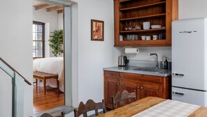 A compact kitchen with wooden cabinets, a refrigerator, and a dining area with a table and chairs. - Historic Rumpel Kammer - Steps to Main Street (Fredericksburg)