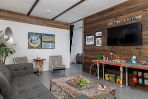 Ein modernes Wohnzimmer mit einer Couch, Sesseln, einem Couchtisch mit Früchten, einem Fernseher und Holzpaneelen an der Wand.
