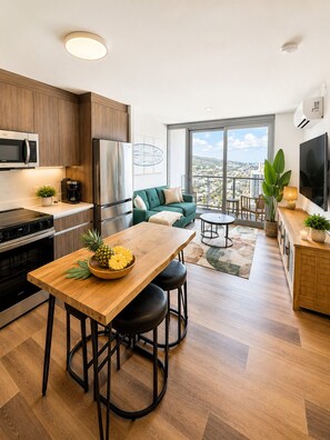 A modern kitchen with a dining area, a living room with a view, and a balcony. - Newly Built High-Floor Condo with Diamond head & Ocean Views & Luxury Amenities (Honolulu)