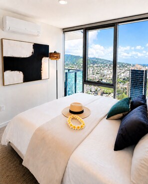 A modern hotel room with a large bed, a city view, and a large abstract painting on the wall. - Newly Built High-Floor Condo with Diamond head & Ocean Views & Luxury Amenities (Honolulu)