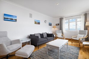 Ein modernes Wohnzimmer mit grauem Sofa, weißem Couchtisch, grauem Sessel und Holzboden.