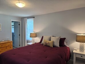 Ein Schlafzimmer mit einem großen Bett, zwei Nachttischlampen, einer Holzkommode und einer Tür zu einem anderen Raum.