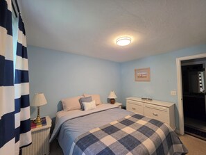 Een slaapkamer met een bed, nachtkastjes, een kaptafel en een deur naar een andere kamer.