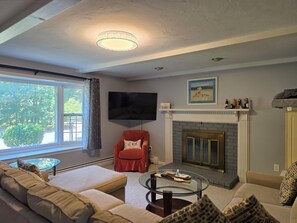 A living room with a sofa, a glass coffee table, a fireplace, a television, and a window with curtains. - 'The Whales Tail' ~ Dogs Welcome (Yarmouth)