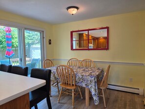 A dining area with a table and chairs, a sliding glass door, and a ceiling light fixture. - 'The Whales Tail' ~ Dogs Welcome (Yarmouth)