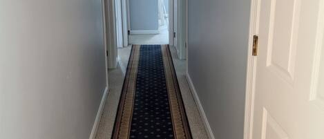 Un pasillo con alfombra estampada, puertas blancas y un ventilador de techo.