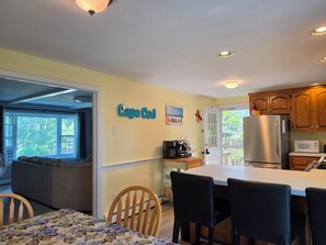A kitchen with a large island, wooden cabinets, a stainless steel refrigerator, and a dining area with chairs and a table. - 'The Whales Tail' ~ Dogs Welcome (Yarmouth)