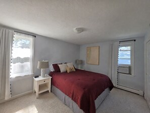 A bedroom with a bed, two bedside tables with lamps, a window with curtains, and a wall-mounted air conditioning unit. - 'The Whales Tail' ~ Dogs Welcome (Yarmouth)