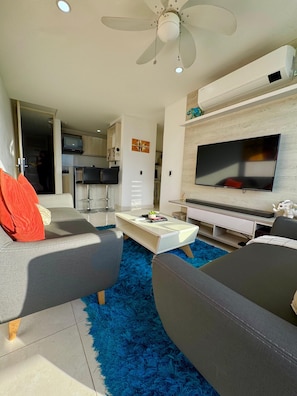 Uma sala de estar moderna com uma TV de tela plana, sofás cinzas, uma mesa de centro e um ventilador de teto.