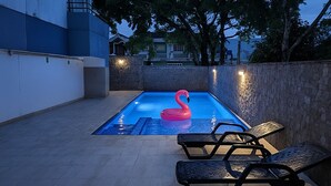 Een zwembad met een roze flamingo drijver, omringd door stenen muren en tuinmeubilair.