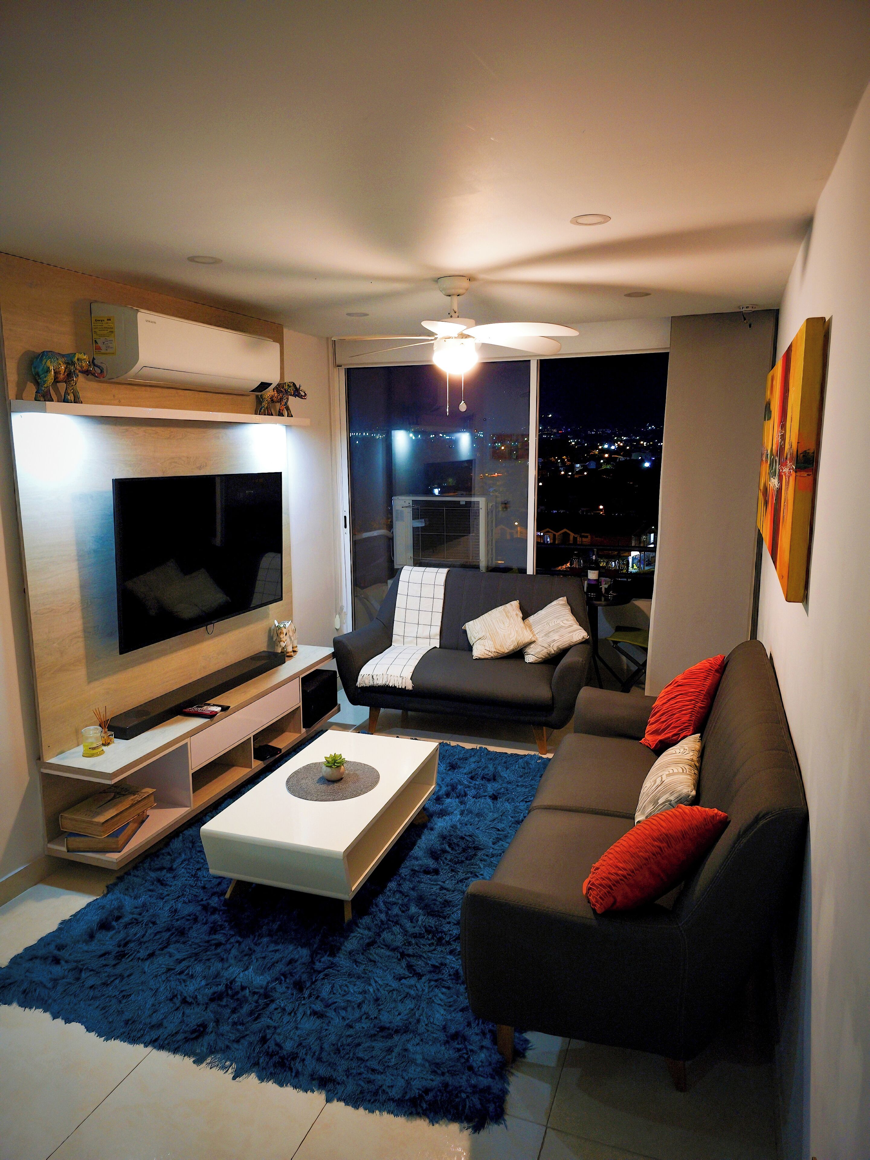Sala moderna com televisão de tela plana, sofá, mesa de centro e vista da cidade à noite.