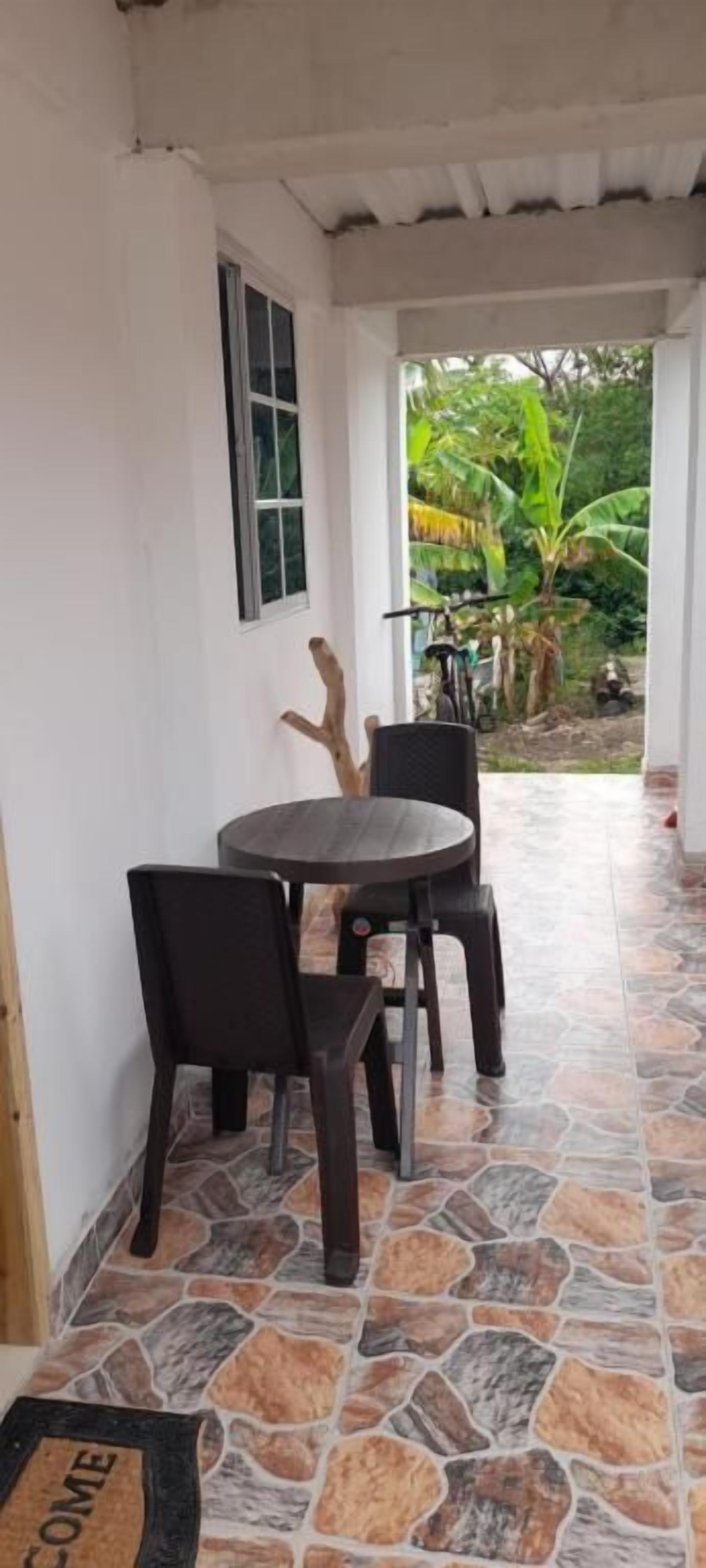 Un espacio de estar techado al aire libre con suelo de piedra, una mesa redonda y cuatro sillas.