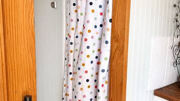 A bathroom with a white door, a wooden door frame, a white cabinet with a black handle, and a shower curtain with multicolored polka dots.