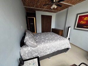 Ein Schlafzimmer mit einem Bett, einem Deckenventilator, einer Tür und einem gerahmten Bild an der Wand.