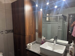 Ein Badezimmer mit Holzwaschtisch, einem großen Spiegel, einem Waschbecken und einer Dusche.
