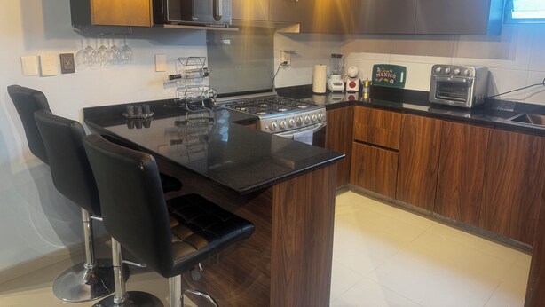 A modern kitchen with a central island, bar stools, a stove, a microwave, and a toaster oven. - Providencia condo rock star location a block from everything (Guadalajara)