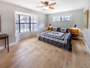 A bedroom with a bed, two windows, a ceiling fan, and a nightstand with a lamp. - Bear Crest W/Spa Near Snow Summit (Big Bear Lake)