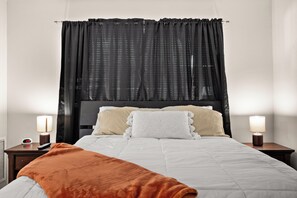 A neatly made bed with a white and orange blanket, two bedside lamps, and a black curtain.