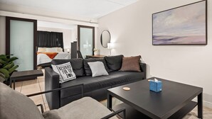 Ett modernt hotellrum med en svart lädersoffa, ett litet bord, en säng med utsikt och en tavla på väggen.
