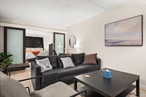 A modern hotel room with a black leather sofa, a small table, a bed with a view, and a painting on the wall. - Modern Condo, Fire Pit,Near Bucs Stadium, Downtown & TPA Airport (Tampa)
