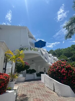 A white building with a curved balcony, a blue umbrella, and red flowers. - Spacious, Family-Friendly Apartment with Ocean Views (Manzanillo)