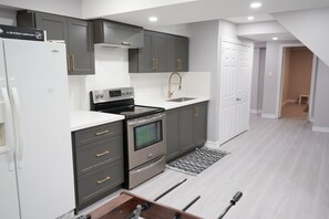 A modern kitchen with grey cabinets, a white countertop, a stainless steel oven, and a sink.