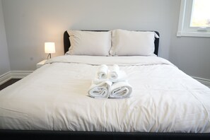 A neatly made bed with white linens and towels, a bedside lamp, and a window with daylight.