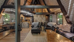 Amplio espacio tipo loft con techo alto, vigas a la vista, una pared de acento de piedra y una zona de estar acogedora con chimenea.