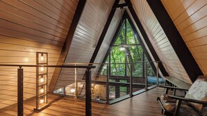 Un interior con techo inclinado, suelo de madera, una zona de estar con sillones de cuero y vistas a zonas verdes.
