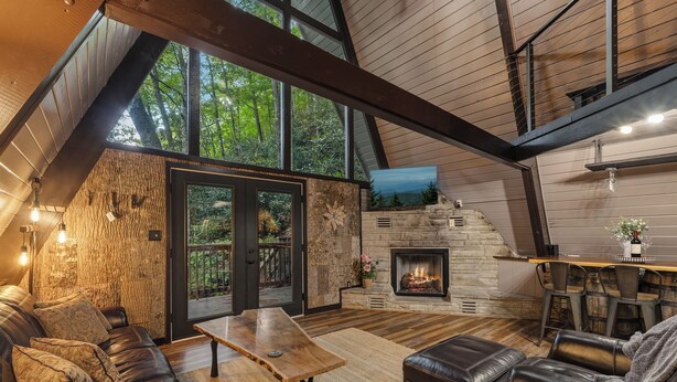 Una sala de estar acogedora con chimenea, mobiliario de cuero y un ventanal con vistas a la vegetación.