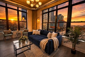 A modern living room with a large window, a blue sofa, a coffee table, and a potted plant. - Modern 2BR/2BA Corner Suite Near McCormick Place (Chicago)