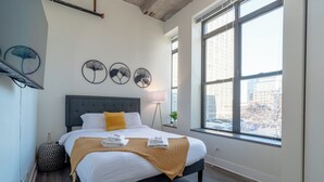 Un dormitorio moderno con una cama grande, una ventana con vista a la ciudad y decoración en la pared.