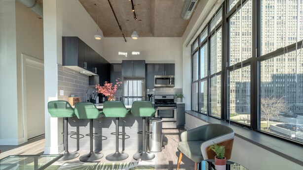Una cocina moderna con armarios oscuros, un microondas de acero inoxidable y un amplio ventanal con vistas a un paisaje urbano.