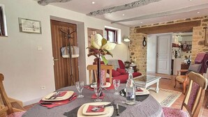 A dining area with a round table set for four, a vase with a flower, and a kitchen visible in the background. - Chez Mamig - GOUDELIN (GOUDELIN)
