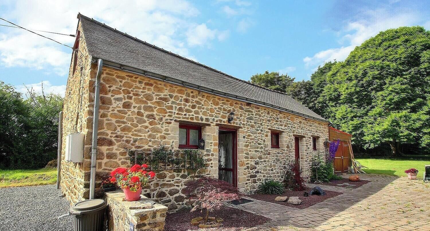 Un edificio de piedra con techo inclinado, un pequeño porche y un jardín con flores rojas.