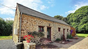 A stone building with a sloped roof, a small porch, and a garden with red flowers. - Chez Mamig - GOUDELIN (GOUDELIN)