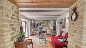 A rustic interior with exposed beams, stone walls, a red sofa, a dining area, and a staircase. - Chez Mamig - GOUDELIN (GOUDELIN)